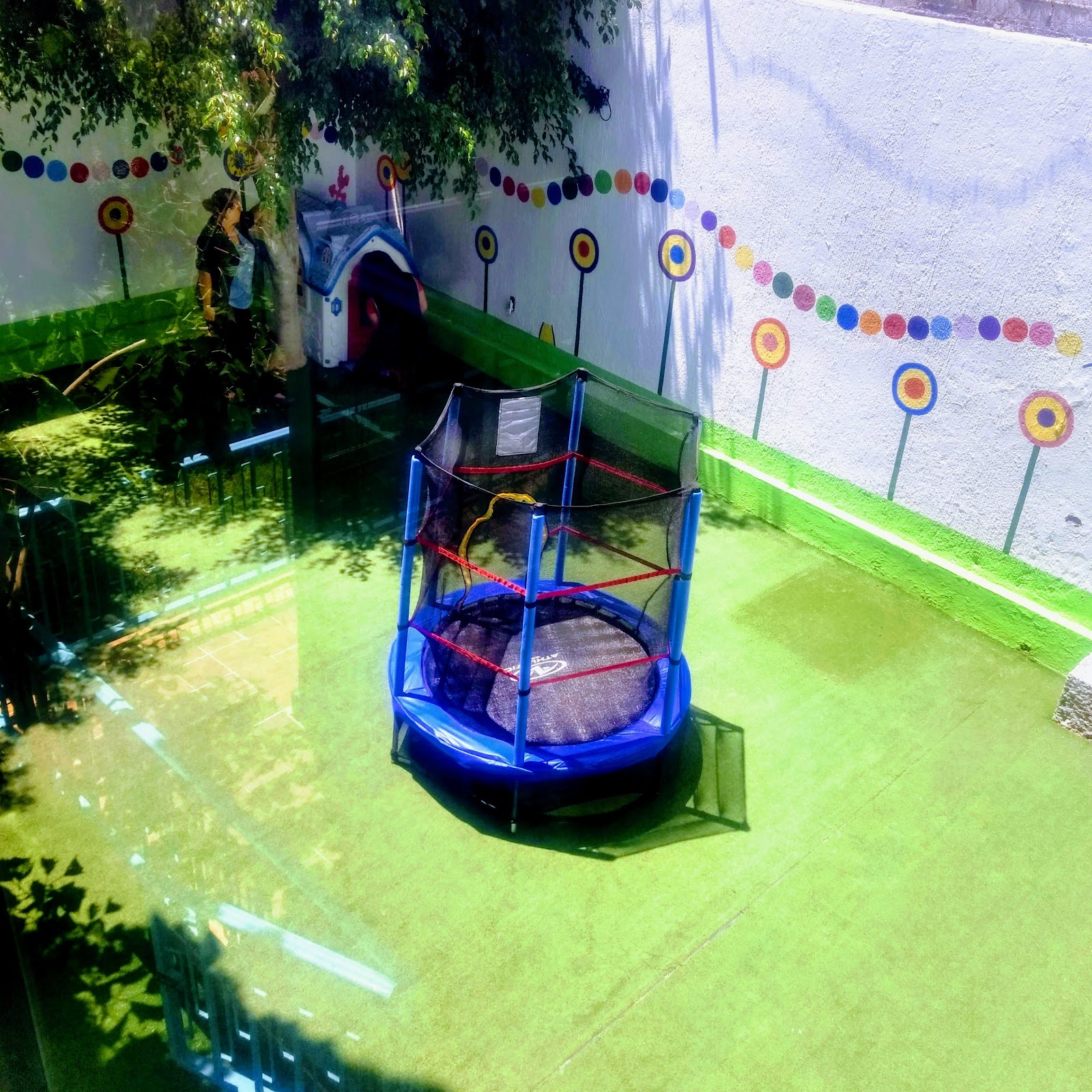 Patio al aire libre de Bügu Guardería con pasto, trampolín y pared de flores pintadas